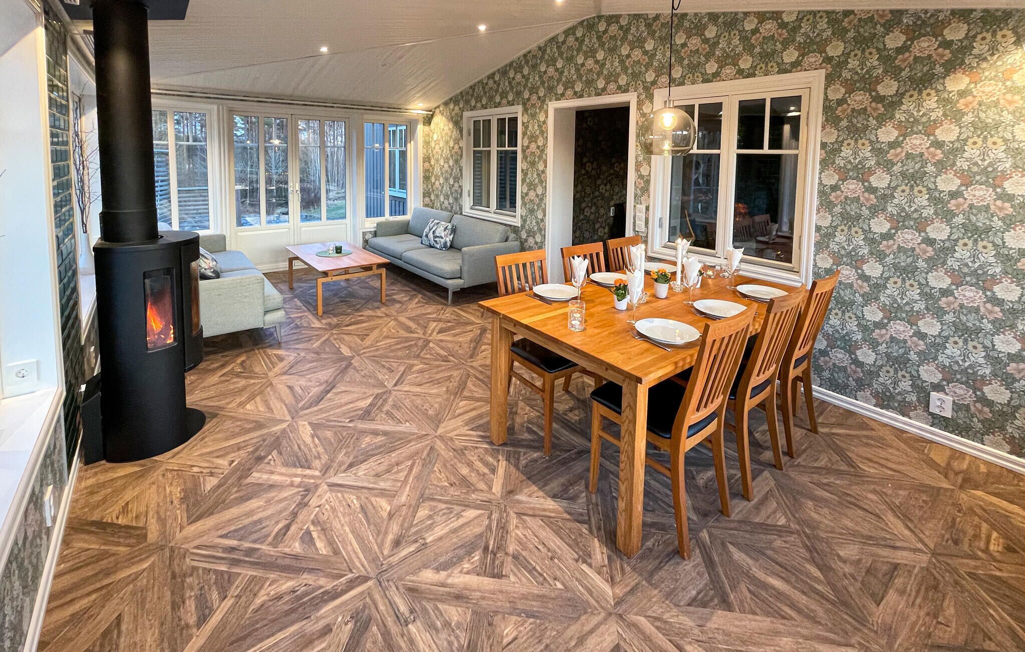 A cozy living room with a fireplace, a dining area with a wooden table and chairs, and a patterned wallpaper.