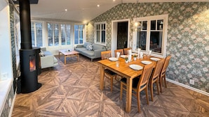 A cozy living room with a fireplace, a dining area with a wooden table and chairs, and a patterned wallpaper.