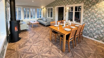 A cozy living room with a fireplace, a dining area with a wooden table and chairs, and a patterned wallpaper.