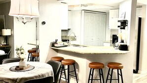 A modern kitchen with a central island, bar stools, a dining table, and a chandelier.