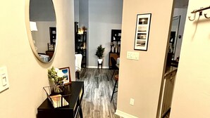 A hallway with a wooden floor, a round mirror, a small table with a basket, and a framed picture on the wall.