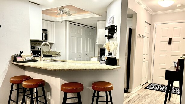 A modern kitchen with a central island, bar stools, and a dining area with a black chair.