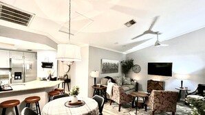 A modern living room with a dining area, a kitchen, and a ceiling fan.