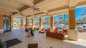 A covered outdoor seating area with red and brown wicker furniture, a pool view, and a signboard. - Regal Oaks Townhouse - September Special Price! (Kissimmee)