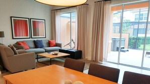 A modern living room with a wooden dining table, sofas, and a large window with curtains. - Regal Oaks Townhouse - September Special Price! (Kissimmee)