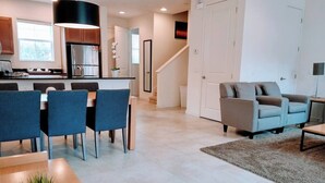 A modern kitchen with a central island, dining area with chairs, a sofa, and a staircase leading to another level. - Regal Oaks Townhouse - September Special Price! (Kissimmee)