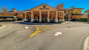 Un hôtel appelé Regal Oaks, doté d’une entrée abritée, d’un parking avec des flèches indiquant les directions et surplombant un ciel d’un bleu limpide.