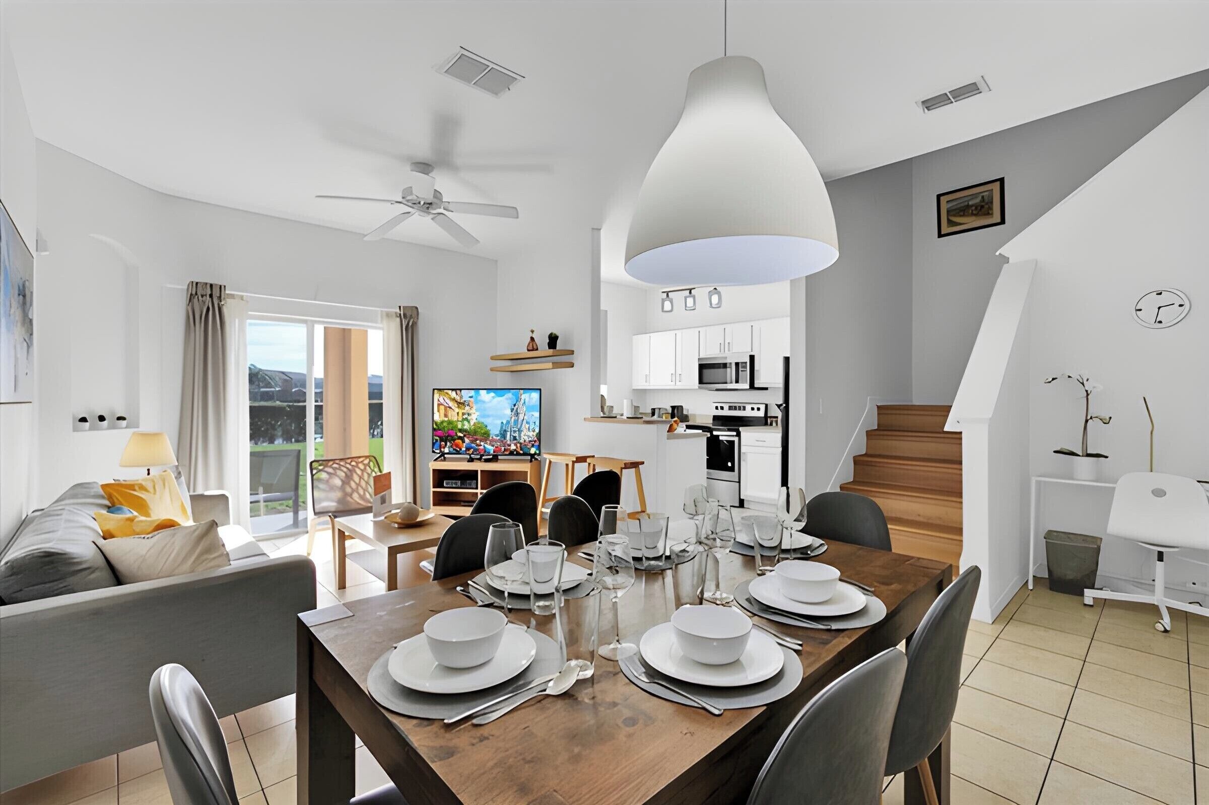 A modern living room with a dining area, a kitchen, and a staircase.