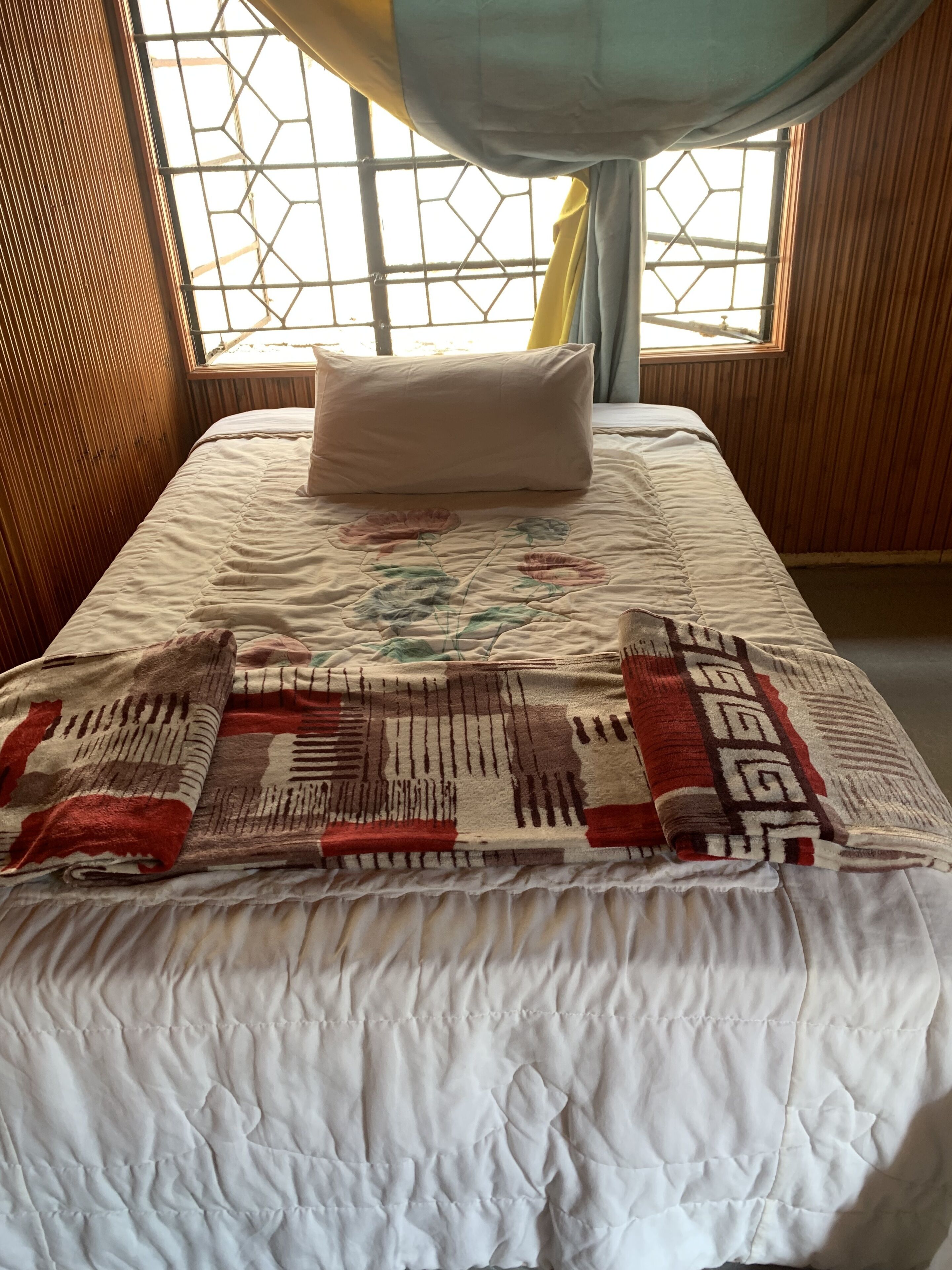 A bed with a quilt, a pillow, and a window with a curtain.