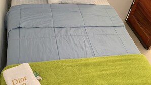 Un lit bien fait, avec une couette bleue, un plaid vert et une serviette blanche de la marque Dior Beauty.