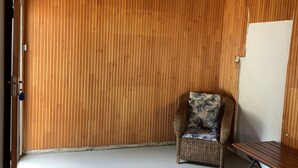 Une pièce avec un mur lambrissé en bois, une chaise en osier avec un coussin à motifs floraux, un banc en bois et un tapis à motifs.