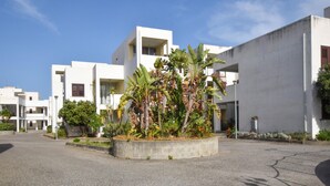 A modern building complex with white exteriors and a central garden area with tropical plants. - Cozy apartment in Isca Marina with WiFi (Isca Marina)