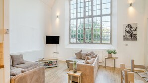 Ein geräumiges Wohnzimmer mit großem Fenster, einem Flachbildfernseher und einem Gemälde an der Wand.