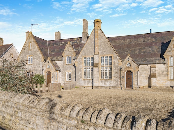 A stone building with multiple chimneys, a wooden fence, and a gravel ground.