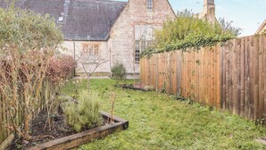 Ein Steinhaus mit einem dreieckigen Dach, einem Holzzaun und einem Garten mit verschiedenen Pflanzen.