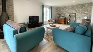 Una sala de estar moderna con sofás color turquesa, un televisor, una chimenea y una pared con diseño de piedra.