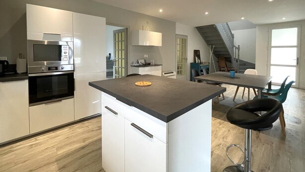Una cocina moderna con electrodomésticos integrados, una isla central y un comedor con una escalera que conduce a un nivel superior.