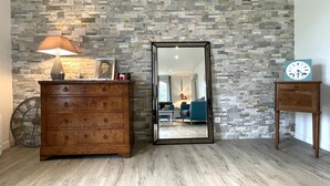 Una habitación con pared de piedra, un aparador de madera con cajones, un espejo, un reloj y una lámpara.