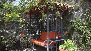Un jardín con una silla colgante de metal, una planta en maceta y un muro de piedra.