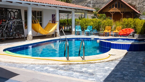 Una piscina con suelo de baldosas, una hamaca y mobiliario de exterior.
