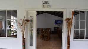 Una habitación con piso de baldosas, un sofá, un televisor y dos jarrones altos con plantas secas.