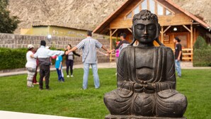 Una estatua de Buda en un parque, con un edificio de madera al fondo.