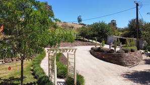 A gravel driveway leading to a gated entrance with a pergola, surrounded by landscaped gardens and a stone wall. - Beautifully renovated country cottage located near Mclaren Vale's best wineries (Clarendon)