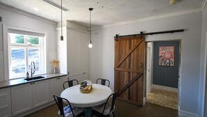 A kitchen with a round table, chairs, a hanging light fixture, a window, and a wooden barn door. - Beautifully renovated country cottage located near Mclaren Vale's best wineries (Clarendon)