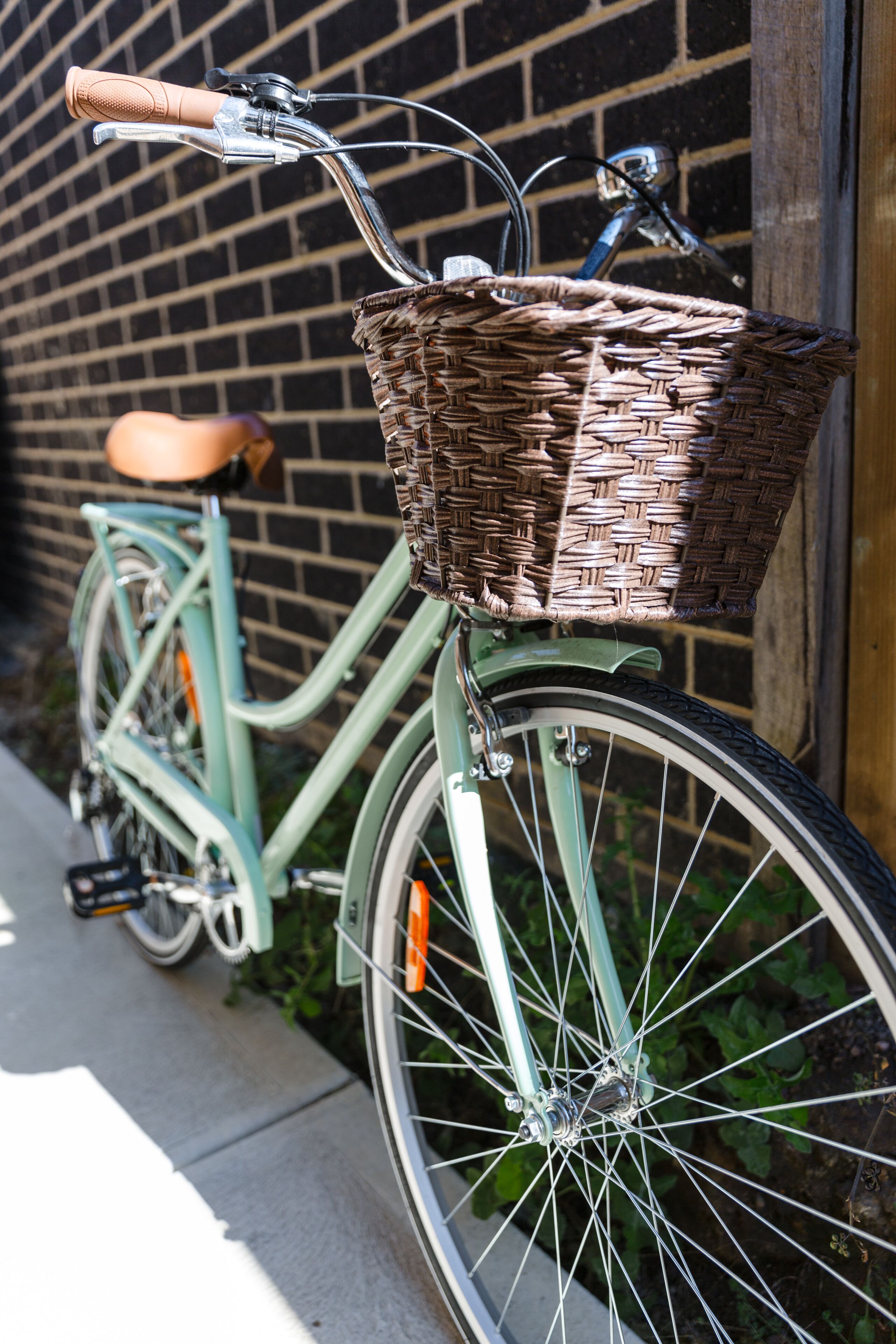 A vintage bicycle with a wicker basket attached to the front, parked against a brick wall.