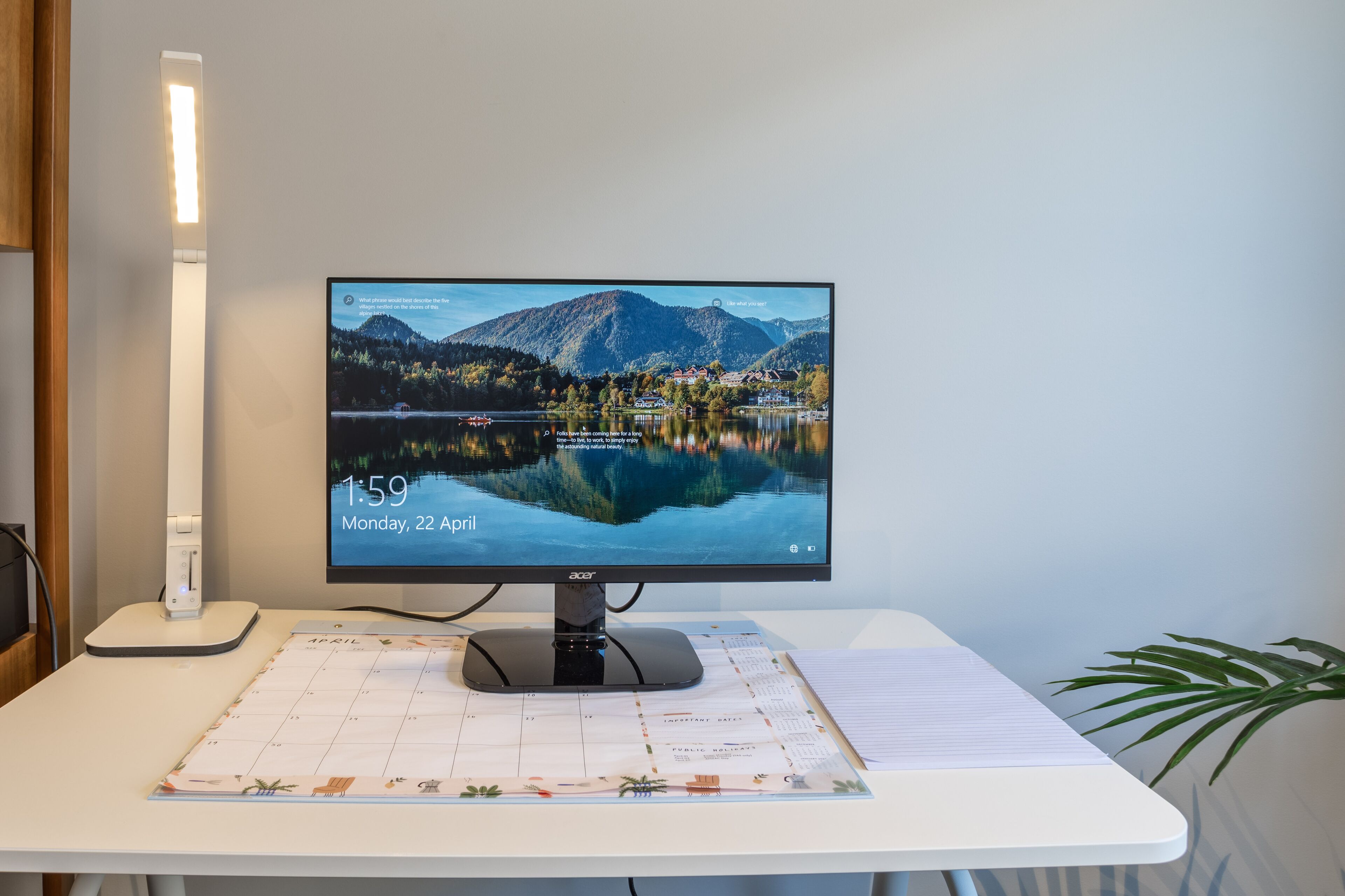 A computer monitor on a desk with a calendar and a lamp.