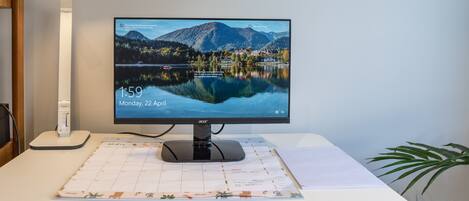 A computer monitor on a desk with a calendar and a lamp.