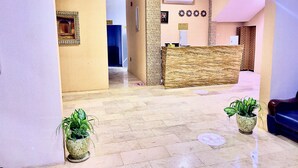 A reception area with a marble floor, a reception desk, potted plants, and a blue couch. - Royal Beach Hotel (Shinas)