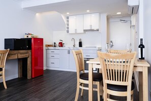 A compact kitchen with white cabinets, a red microwave, and a wooden dining table with chairs.