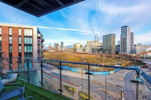 Un edificio moderno con balcón de vidrio que da a una vista panorámica de la ciudad, incluyendo un sitio de construcción y una autopista.