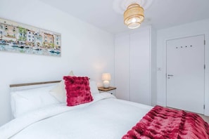 Un dormitorio con una cama, una mesita de noche, una lámpara, una puerta y un cuadro colgado en la pared.