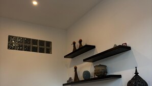 Un área de comedor moderna con una mesa y sillas de vidrio, paredes blancas y estantes decorativos con diversos objetos.