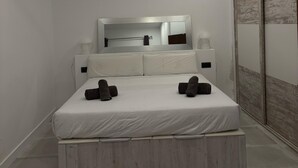 Un dormitorio moderno con cama, ventilador de techo, espejo grande y puerta corredera.