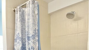 Ein Duschbereich mit gemustertem Duschvorhang, einer Handbrause und einem gefliesten Boden mit Kieselmuster.