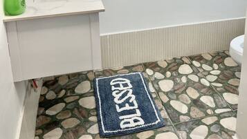 Une salle de bain avec un lavabo blanc, une bouteille verte, une fenêtre en blocs de verre bleus et un sol en mosaïque.