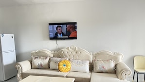 Ein Wohnzimmer mit einem cremefarbenen Sofa, passendem Hocker, einem kleinen weißen Tisch und einem an der Wand montierten Fernseher.