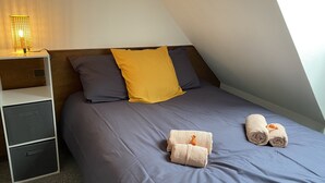 Een slaapkamer met een bed, twee kussens, een nachtkastje, een lamp en twee handdoeken.