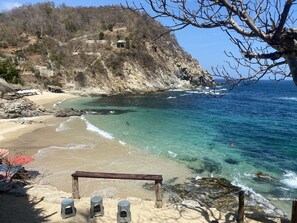 A beach with clear turquoise water, rocky cliffs, and a few people swimming.
