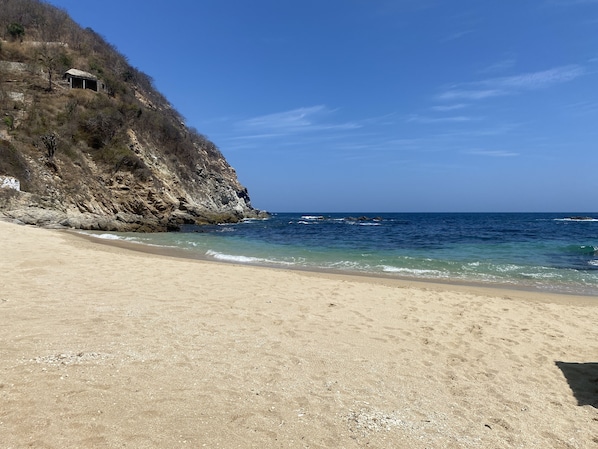A beach with a rocky cliff and a small building on top.