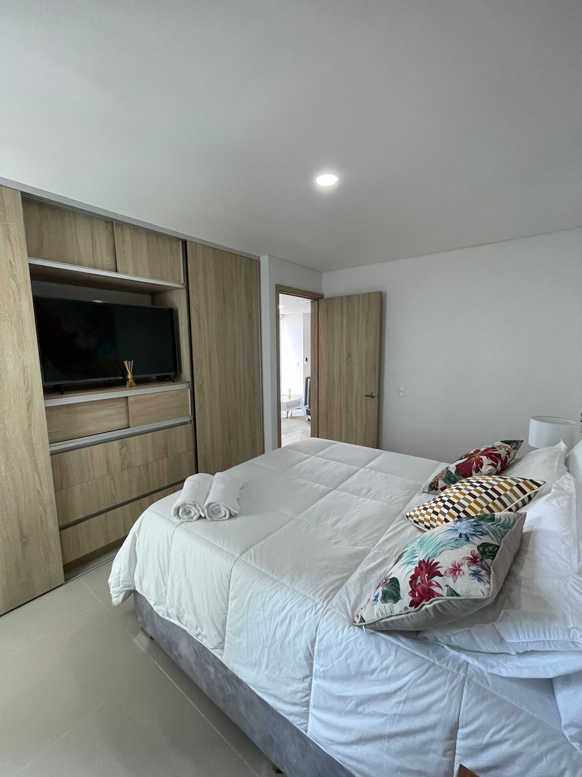 Une chambre à coucher moderne avec un grand lit, un téléviseur posé sur un meuble en bois et une vue sur l’extérieur.