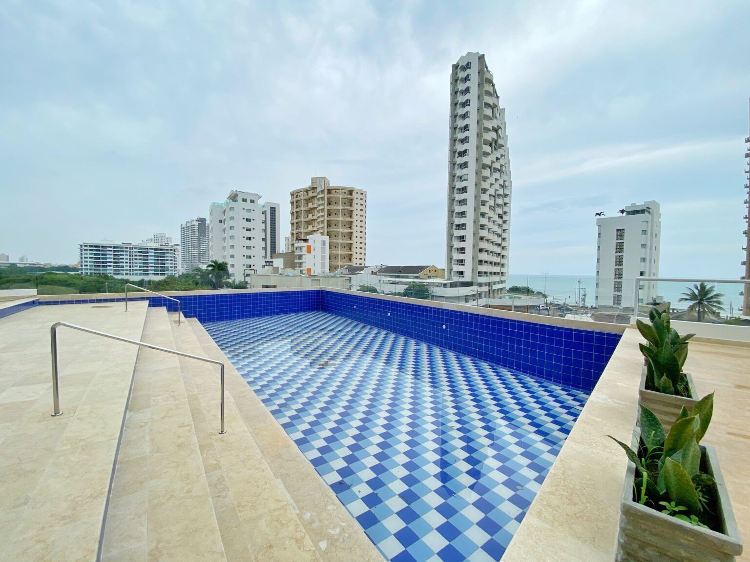A rooftop pool with blue and white checkered tiles, surrounded by a metal railing.