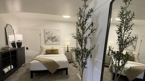 Um quarto com cama, mesas de cabeceira, cômoda, espelho e duas plantas em vasos.