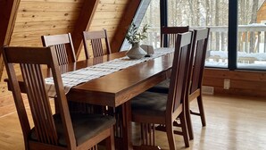 A wooden dining area with a high ceiling and large windows overlooking a snowy landscape. - Apres’ Haus: Comfy A-Frame centrally located in Whitecap Village with fireplace  (Upson)
