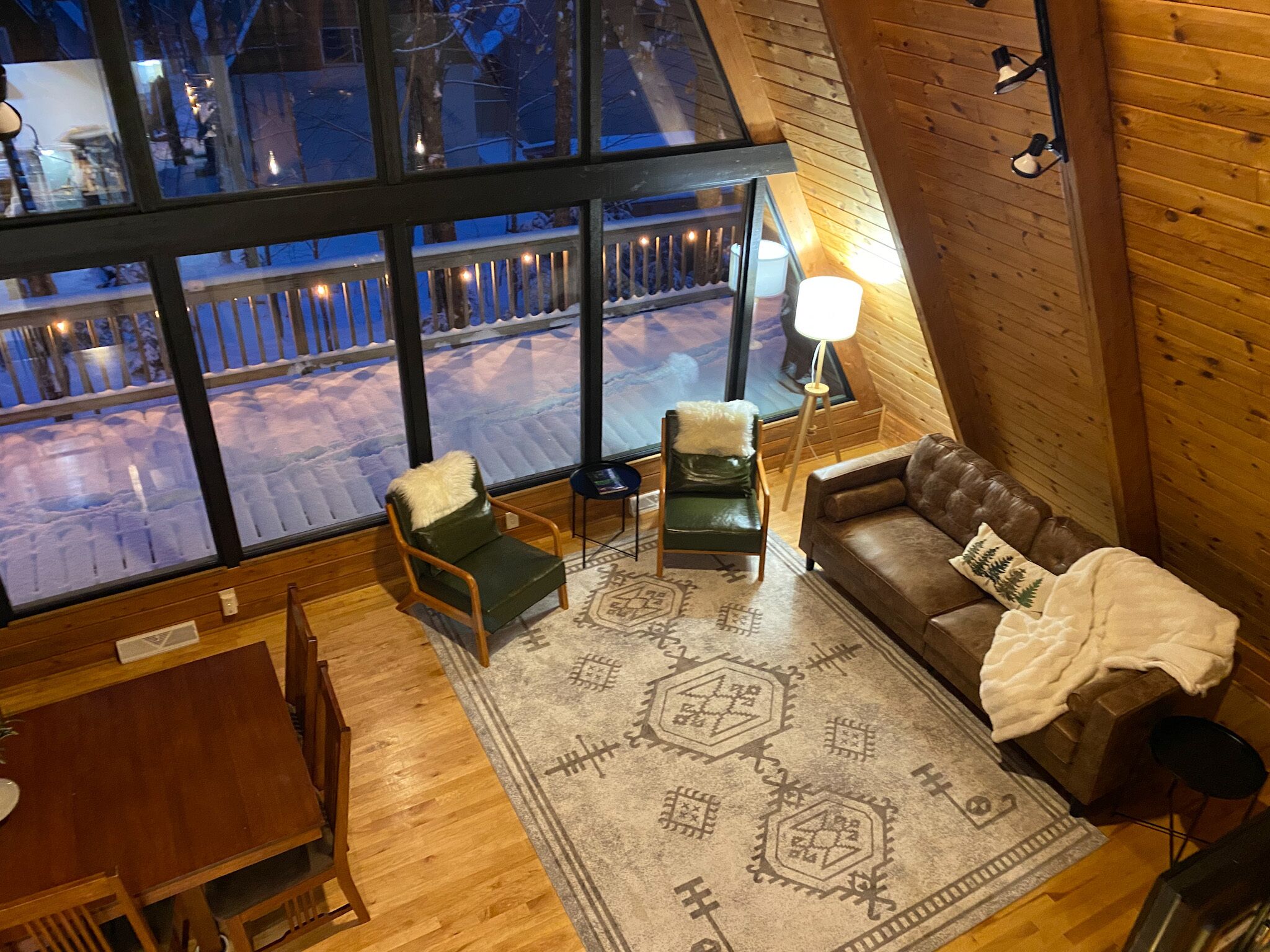 Une pièce chaleureuse avec une grande fenêtre, un canapé en cuir marron, un fauteuil vert et un tapis à motifs.