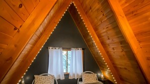 A cozy attic bedroom with two beds, wooden sloped ceilings, and string lights. - Apres’ Haus: Comfy A-Frame centrally located in Whitecap Village with fireplace  (Upson)