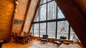 A cozy, wooden interior with a large window offering a view of a snowy landscape. - Apres’ Haus: Comfy A-Frame centrally located in Whitecap Village with fireplace  (Upson)